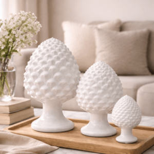 Trois modèles de pomme de pin en céramique blanches sur étagère en salon.